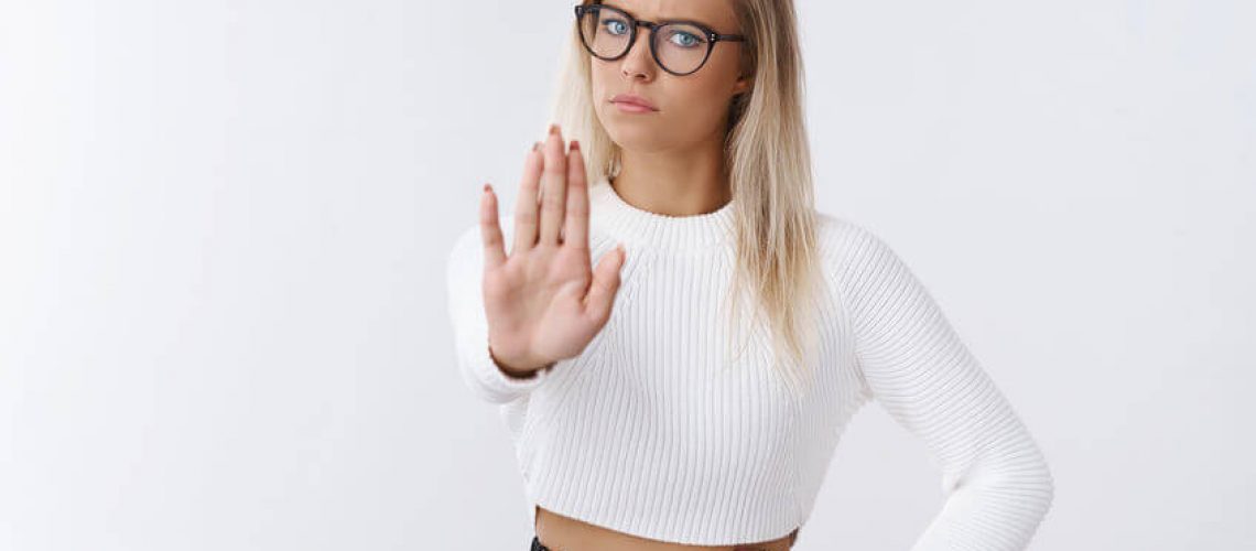 Stop right there. Upset displeased serious-looking powerful fai-haired businesswoman in glasses and trendy outfit pulling palm towards camera in forbidden and no gesture frowning dissatisfied.